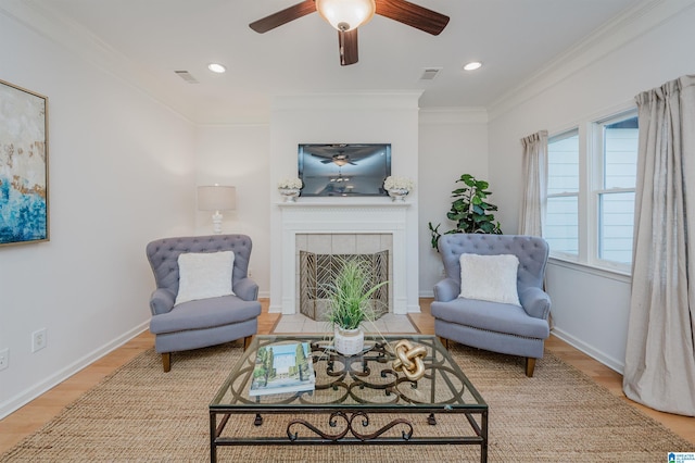 living area featuring a tile fireplace, crown molding, ceiling fan, and hardwood / wood-style flooring