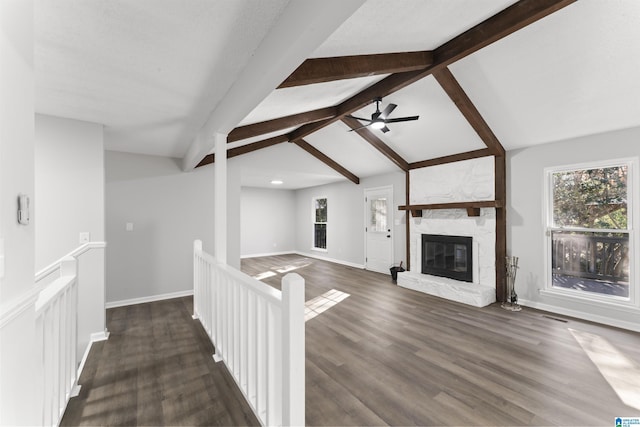 unfurnished living room with vaulted ceiling with beams, a stone fireplace, ceiling fan, and dark wood-type flooring