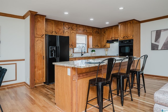 kitchen with crown molding, a center island, black appliances, and light hardwood / wood-style floors