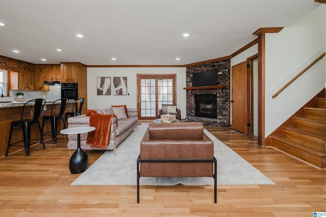 living room featuring a fireplace, crown molding, light hardwood / wood-style flooring, and sink