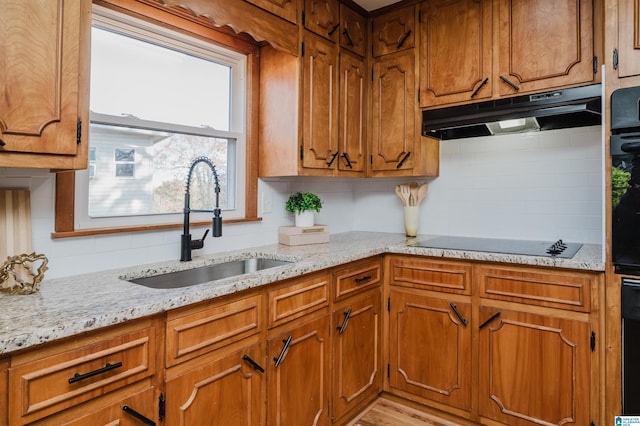 kitchen featuring black electric stovetop, backsplash, light stone counters, and sink