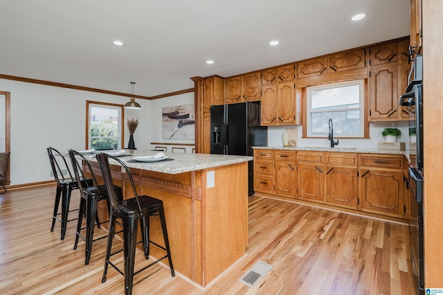 kitchen featuring a kitchen bar, light wood-type flooring, black appliances, sink, and a kitchen island