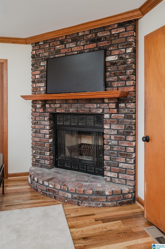 interior details featuring hardwood / wood-style flooring, ornamental molding, and a brick fireplace