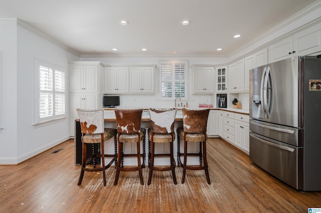 kitchen with a center island, stainless steel fridge with ice dispenser, hardwood / wood-style floors, a breakfast bar, and white cabinets