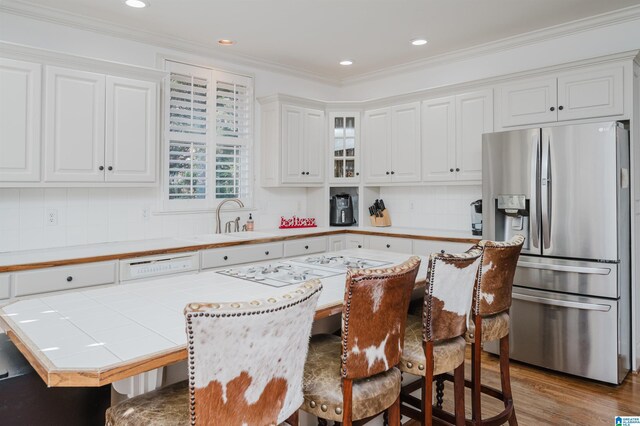 kitchen featuring a kitchen bar, stainless steel fridge, backsplash, ornamental molding, and white cabinetry