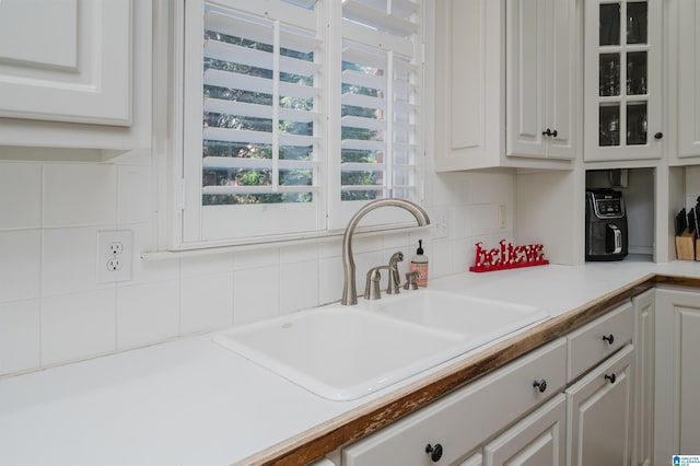 kitchen with backsplash, white cabinetry, and sink