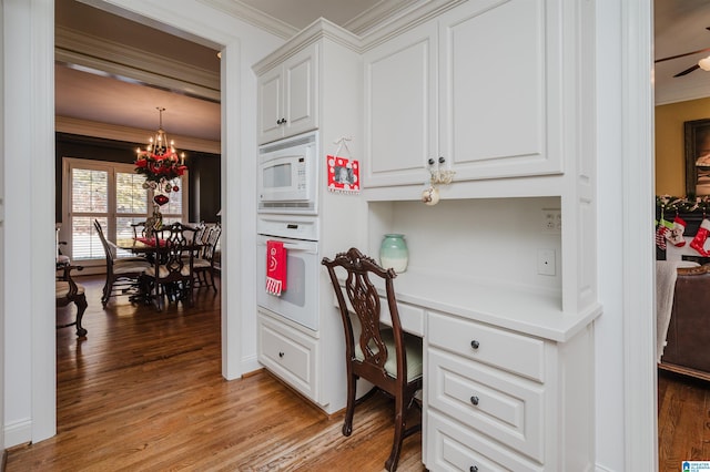 home office featuring built in desk, light wood-type flooring, ceiling fan with notable chandelier, and ornamental molding