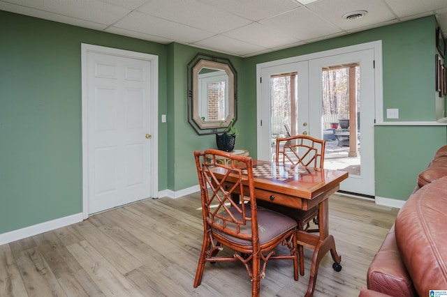 dining area featuring french doors, a drop ceiling, and light wood-type flooring