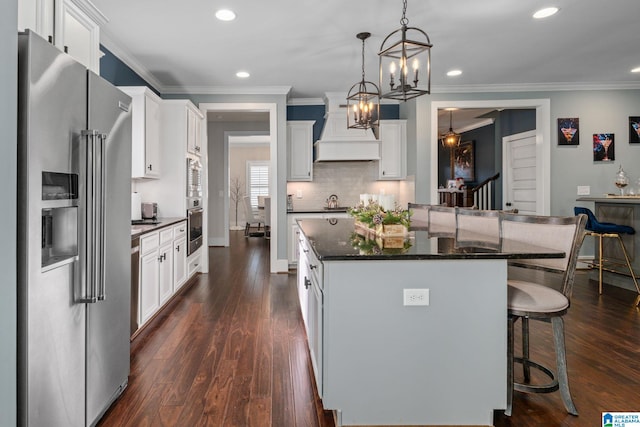 kitchen with white cabinetry, dark wood-type flooring, stainless steel appliances, decorative light fixtures, and custom range hood