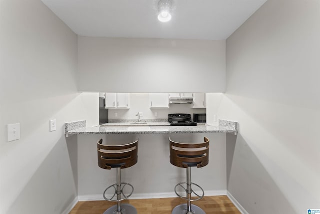 kitchen with black appliances, light hardwood / wood-style flooring, light stone countertops, white cabinetry, and a breakfast bar area