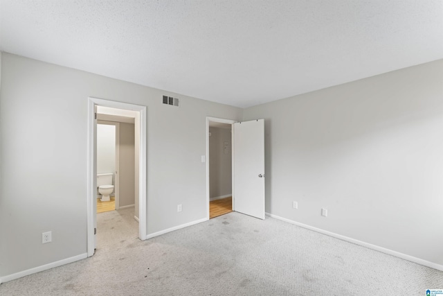 unfurnished bedroom with a textured ceiling, light carpet, and ensuite bath