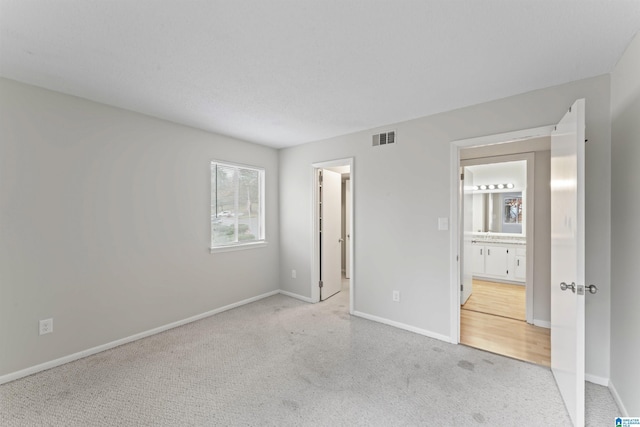 unfurnished bedroom featuring light carpet and connected bathroom