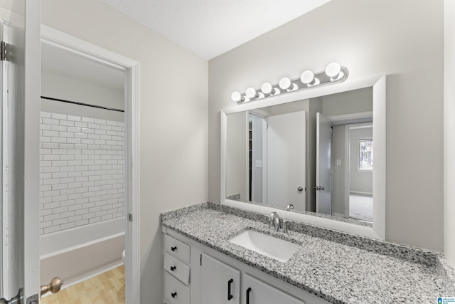 full bathroom with a textured ceiling, vanity, tiled shower / bath combo, hardwood / wood-style flooring, and toilet