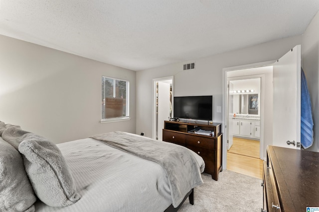 carpeted bedroom with ensuite bath and a textured ceiling