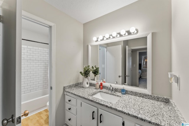 full bathroom with tiled shower / bath, wood-type flooring, vanity, toilet, and a textured ceiling