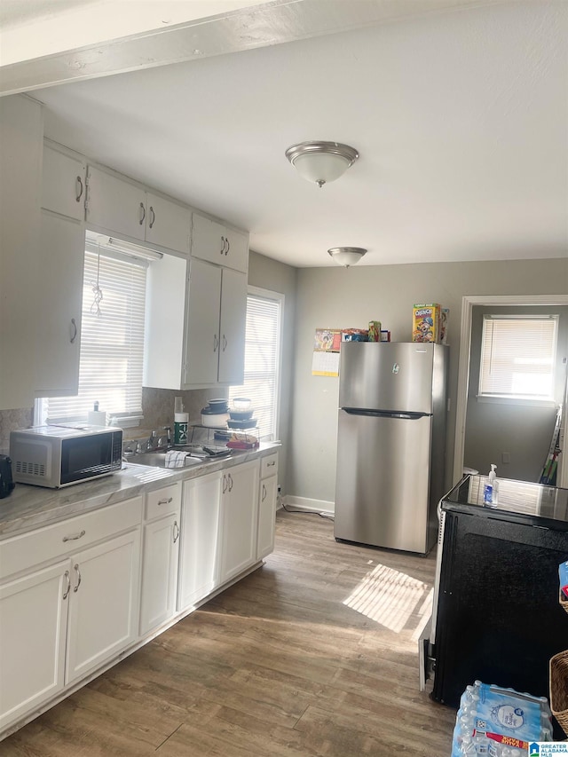 kitchen with decorative backsplash, wood-type flooring, stainless steel refrigerator, white cabinets, and sink