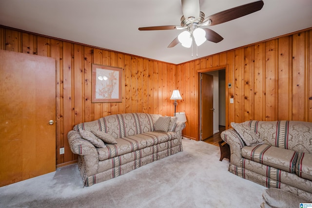 carpeted living room with ceiling fan, ornamental molding, and wood walls