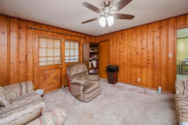 sitting room featuring wood walls, ceiling fan, and light carpet