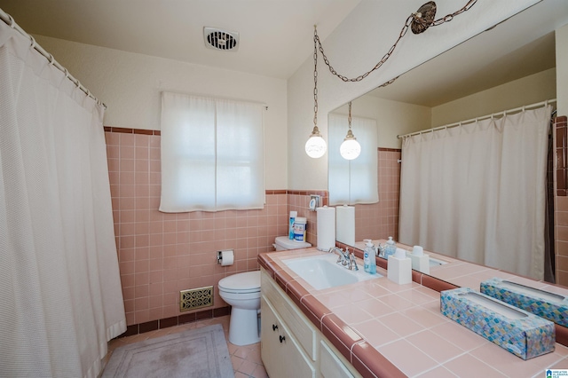 bathroom with tile patterned flooring, vanity, toilet, and tile walls