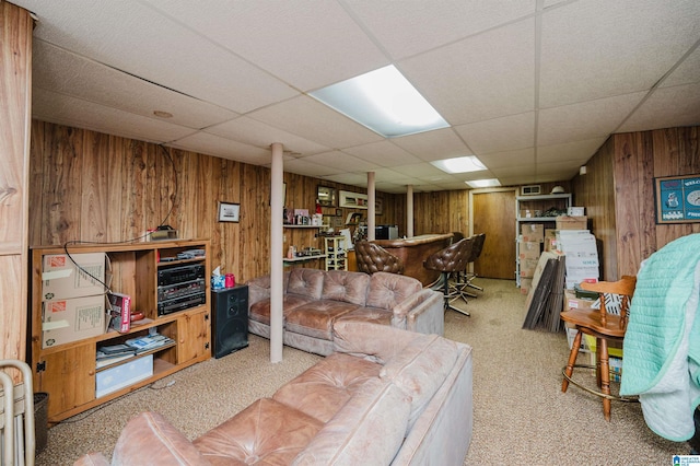 living room with light colored carpet, a drop ceiling, and wood walls