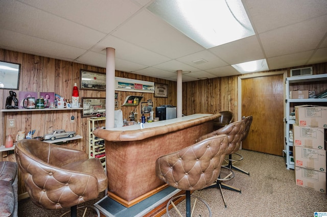 bar with carpet flooring, a drop ceiling, and wooden walls