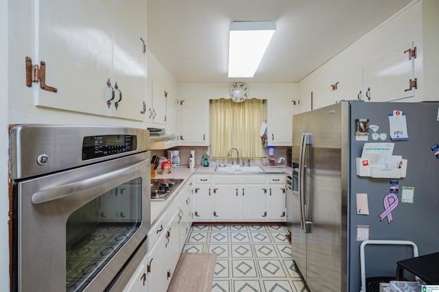 kitchen featuring appliances with stainless steel finishes, range hood, white cabinetry, and sink