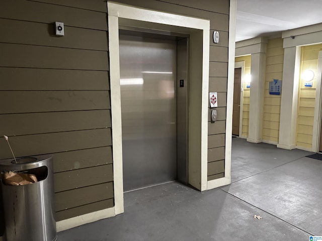 interior space with concrete flooring, elevator, and wood walls