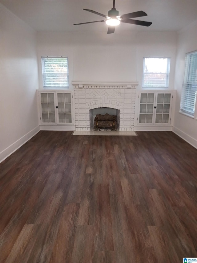 unfurnished living room with ceiling fan, plenty of natural light, dark wood-type flooring, and a brick fireplace