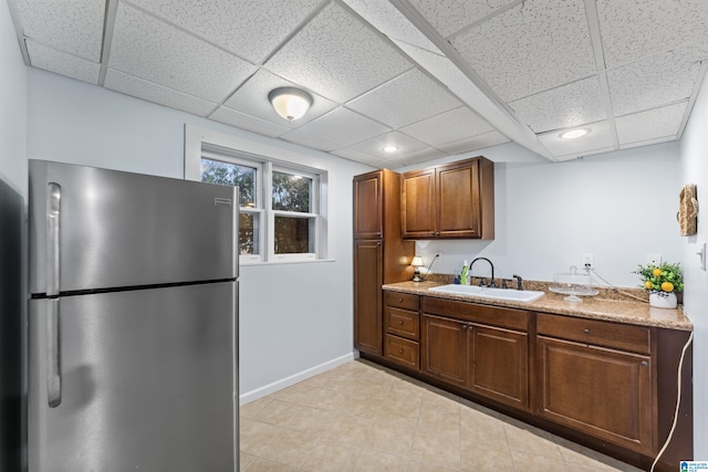 kitchen with light stone countertops, sink, stainless steel fridge, a paneled ceiling, and light tile patterned floors