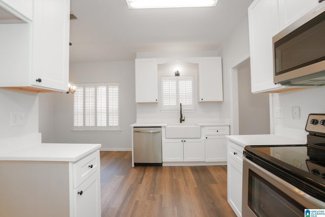 kitchen with white cabinetry, sink, hanging light fixtures, stainless steel appliances, and dark hardwood / wood-style floors