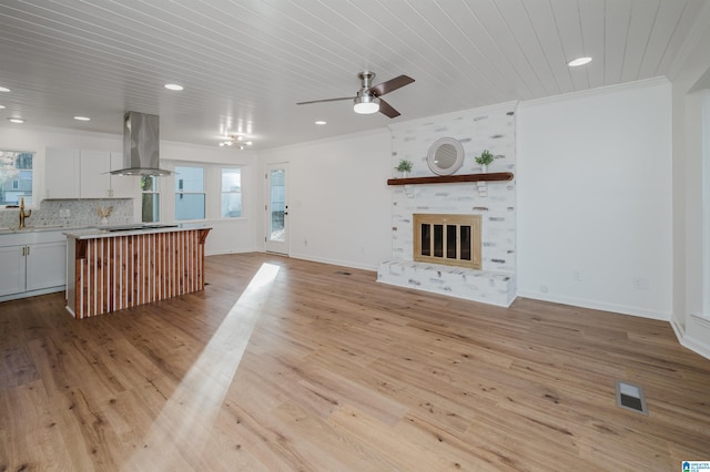 unfurnished living room with ornamental molding, a large fireplace, ceiling fan, sink, and light hardwood / wood-style flooring