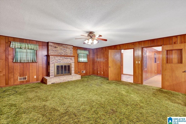 unfurnished living room with carpet flooring, ceiling fan, a fireplace, and wooden walls