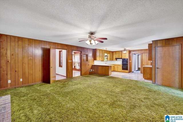 kitchen featuring kitchen peninsula, light colored carpet, a textured ceiling, decorative light fixtures, and wooden walls