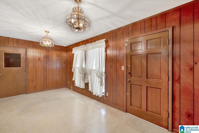 entrance foyer with a chandelier, a textured ceiling, and wood walls