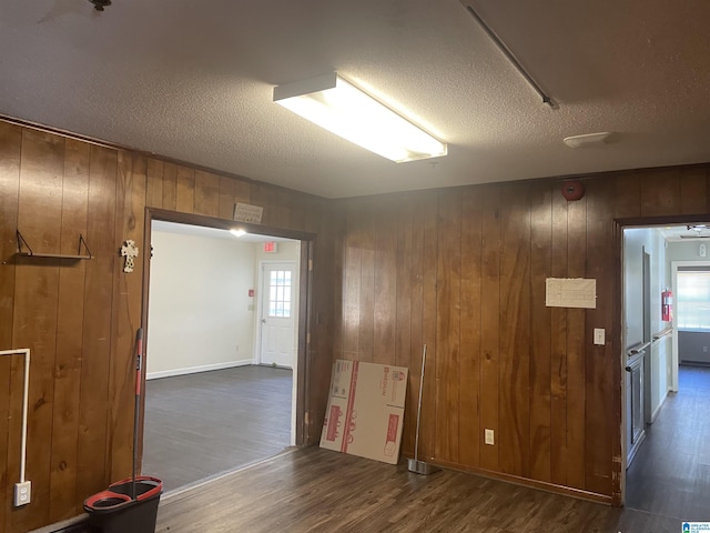 empty room with a textured ceiling, dark wood-type flooring, and wooden walls