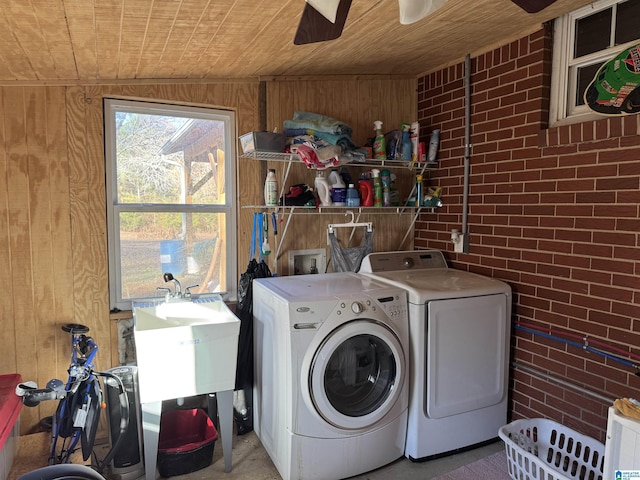 laundry area featuring washing machine and clothes dryer, ceiling fan, brick wall, wooden walls, and wood ceiling