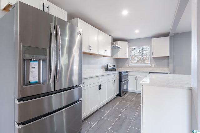 kitchen featuring light stone countertops, appliances with stainless steel finishes, white cabinetry, and wall chimney range hood