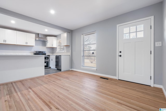 kitchen with white cabinetry, light hardwood / wood-style floors, wall chimney range hood, and appliances with stainless steel finishes