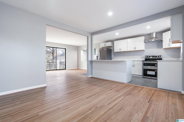 kitchen with white cabinets, stainless steel appliances, light hardwood / wood-style flooring, and wall chimney range hood