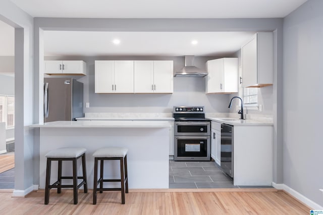 kitchen featuring sink, wall chimney range hood, light hardwood / wood-style floors, white cabinets, and appliances with stainless steel finishes