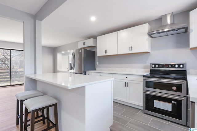 kitchen featuring white cabinets, appliances with stainless steel finishes, a kitchen island, and wall chimney exhaust hood