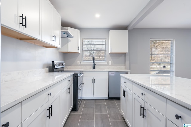 kitchen with light stone counters, wall chimney exhaust hood, stainless steel appliances, sink, and white cabinetry