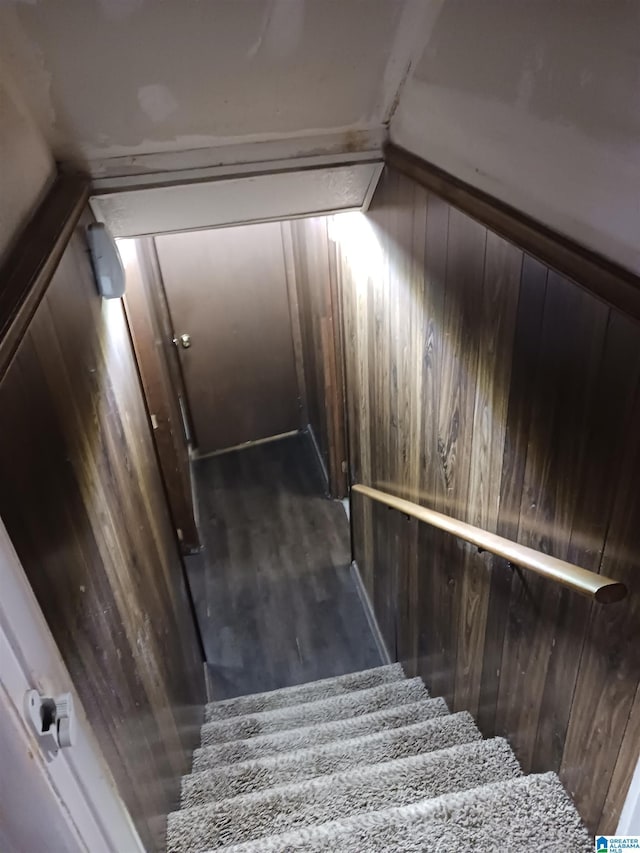 stairway featuring hardwood / wood-style floors, wooden walls, and vaulted ceiling