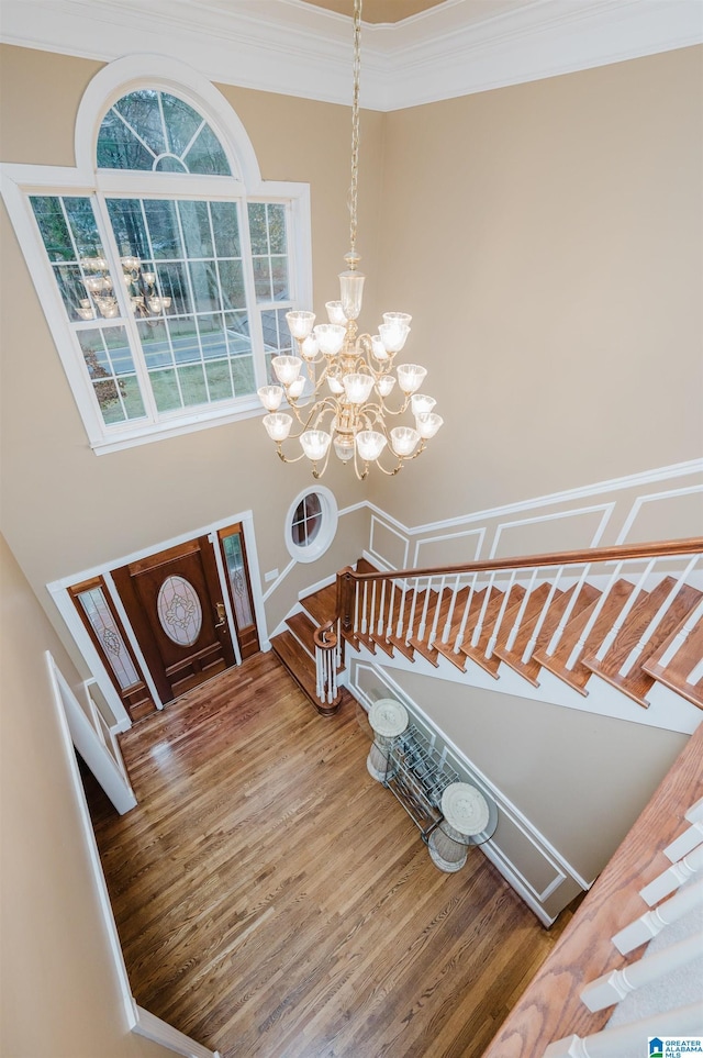 staircase with crown molding, hardwood / wood-style floors, and an inviting chandelier