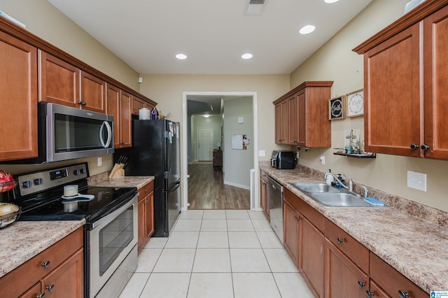 kitchen featuring light tile patterned flooring, appliances with stainless steel finishes, light stone counters, and sink