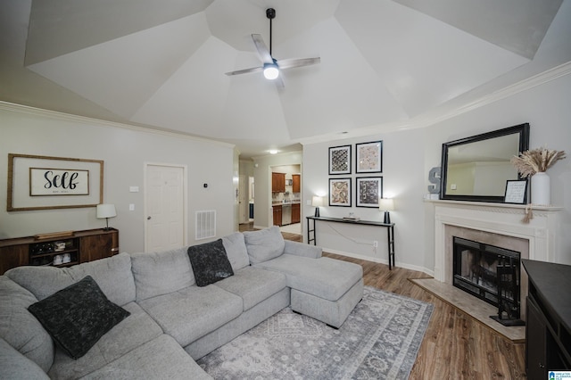 living room featuring hardwood / wood-style floors, lofted ceiling, crown molding, ceiling fan, and a fireplace