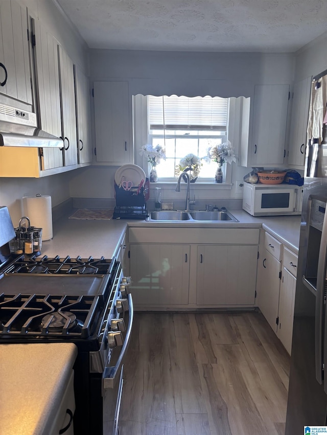 kitchen with wood-type flooring, sink, white cabinetry, and stainless steel appliances