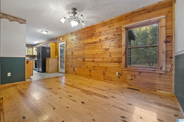 interior space with wood walls, a textured ceiling, and light hardwood / wood-style flooring