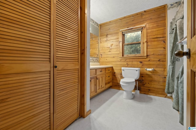 bathroom with vanity, a textured ceiling, toilet, and wooden walls