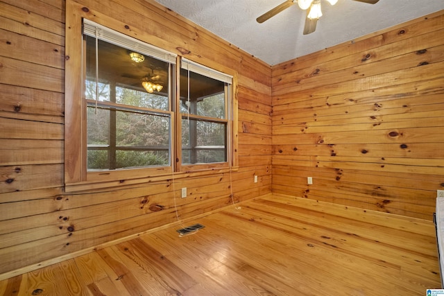 spare room with a textured ceiling, hardwood / wood-style flooring, ceiling fan, and wood walls